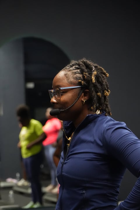 Woman wearing glasses and headset in profile, navy long-sleeve top, with blurred people in background